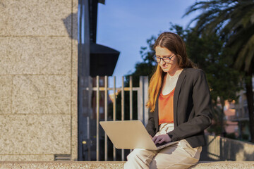 Businesswoman in casual clothes using laptop sitting outdoors