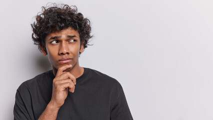 Studio portrait of young thoughtful Hindu man standing on left on white background in black t shirt...