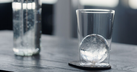man put clear ice ball in tumbler glass on black oak table - obrazy, fototapety, plakaty