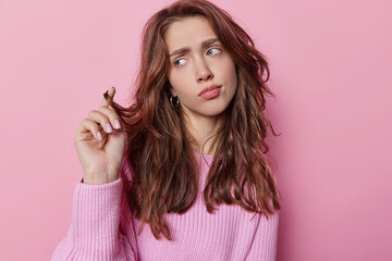 Horizontal shot of woman looks pensively aside has discontent expression dressed in knitted jumper being deep in thoughts isolated over pink background. Pensive lovely female model concentrated aside - obrazy, fototapety, plakaty