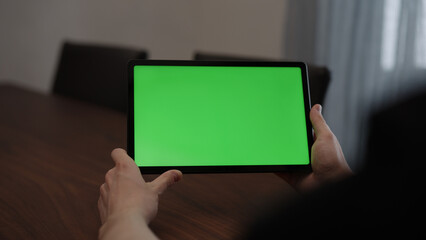 Man at home using tablet pc with green screen while sitting at the table