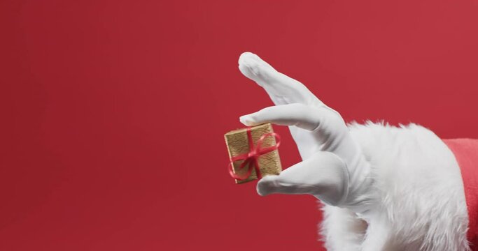 Video of santa claus holding christmas present with copy space on red background