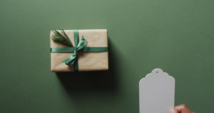 Video of christmas presents and hand holding white tag with copy space on green background