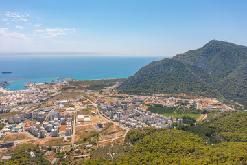 Fototapeta premium Flight over ridge mountain pass rocky terrain with bushes, bird's eye view overlooking the city, houses and buildings, roads and ships, Mediterranean coast, resort area, vacation trip.