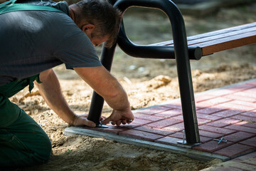 A construction worker bolts a park bench to paving stones.