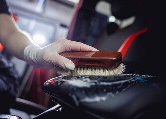 Young woman cleaning the steering wheel of car using a special brush with foam