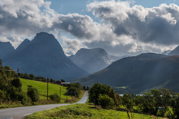 Narrow road leading towards big mountains on a countryside. Lyngen Alps in Norway. Rural landscape.