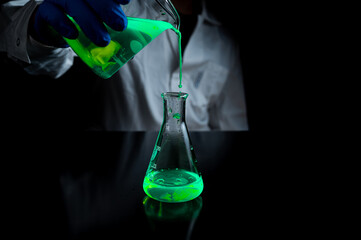 A woman scientist experimenting with a green fluorescent solution in a glass conical flask in dark chemistry laboratory