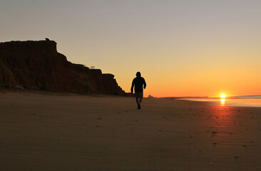 Fototapeta na wymiar Man walking at the sandy beach in beautiful orange color sunrise.