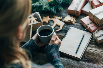 A woman drinks coffee and writes a wish list for Christmas gifts.