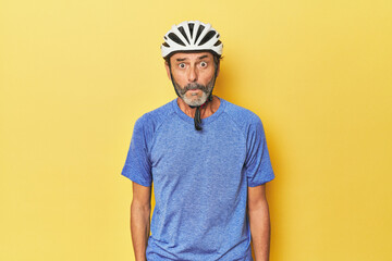 Cyclist wearing helmet in yellow studio shrugs shoulders and open eyes confused.