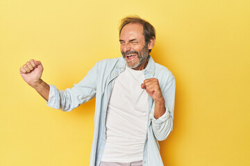 Caucasian middle-aged man in yellow studio dancing and having fun.