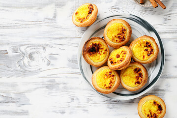 Pastel de nata or Portuguese egg tart. Small tart with a crispy puff pastry crust and a custardy pastry cream filling, top view - obrazy, fototapety, plakaty