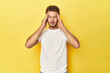 Naklejka premium Young Caucasian man on a yellow studio background touching temples and having headache.
