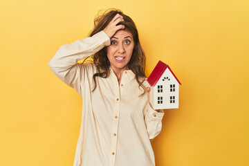 Holding miniature house, realty concept being shocked, she has remembered important meeting.