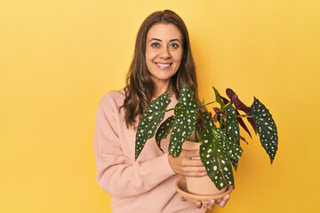 Middle aged woman holding a plant on yellow studio backdrop