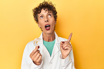 Doctor with invisible dental aligner on yellow pointing upside with opened mouth.