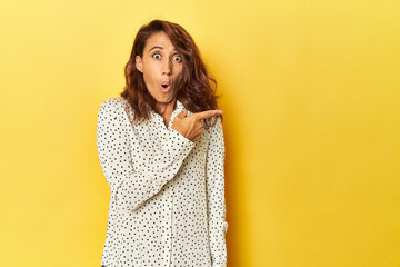 Middle-aged woman on a yellow backdrop pointing to the side