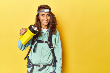 Middle aged woman equipped with backpack, light and lantern on yellow