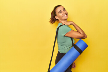 Middle aged athletic woman with yoga mat on yellow