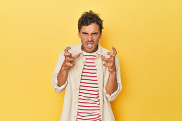 Young Latino man posing on yellow background upset screaming with tense hands.