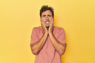 Young Latino man posing on yellow background crying, unhappy with something, agony and confusion concept.