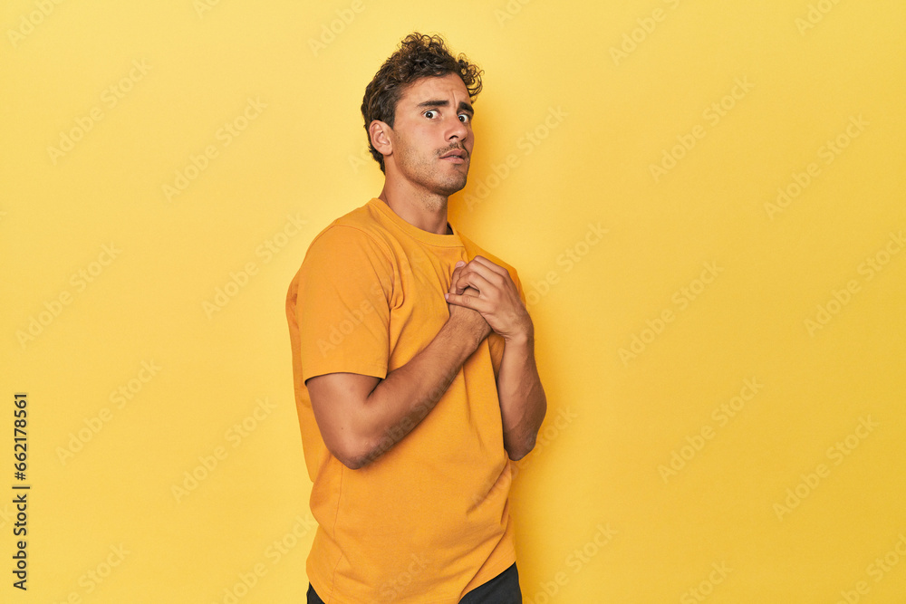 Wall mural Young Latino man posing on yellow background scared and afraid.