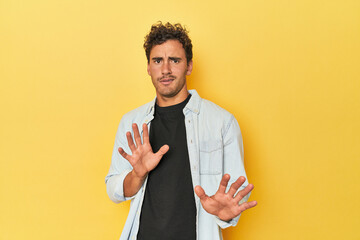 Young Latino man posing on yellow background rejecting someone showing a gesture of disgust.