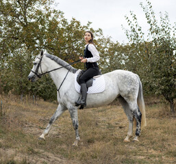 portrait of beautiful woman riding horse in orchard,touches horse muzzle, with forehead glued from animal head.girl calms horse with hand.female and anima in embrace,hugging neck,closed eyes.