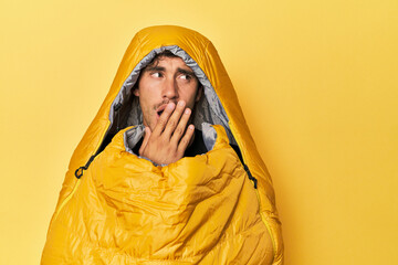 Tired young man in a sleeping bag on yellow.