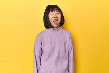 Young Chinese lady, yellow studio background funny and friendly sticking out tongue.