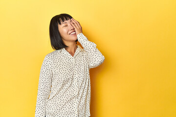 Young Chinese lady, yellow studio background laughing happy, carefree, natural emotion.