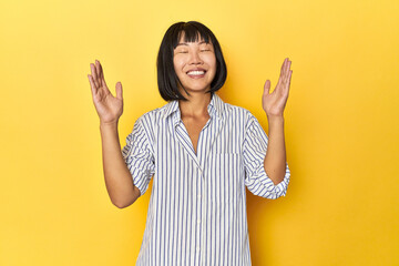 Young Chinese lady, yellow studio background joyful laughing a lot. Happiness concept.