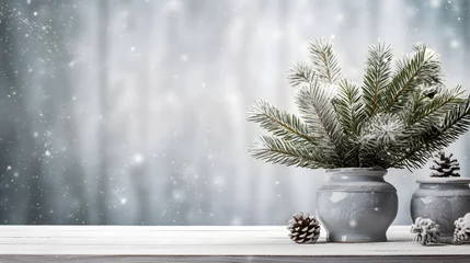 Tuinposter Une composition avec un vase rempli de branches de sapin et des pommes de pin, posés sur une table en bois. En arrière plan, de la neige qui tombe en hiver.  © Gautierbzh