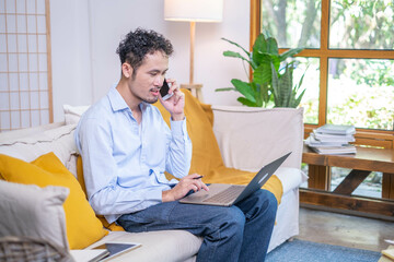 Professional entrepreneur businessman use modern mobile phone technology talking business communication laptop sitting on sofa indoor living room home, adult male man person talking smiling smartphone