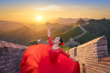 Chinese woman ballet dancer with red dress dancing at sunset in the Great Wall. Woman ballerina dance in ballerina shoes dancing with red silk gown flying on wind and the Great Wall at sunset. China - obrazy, fototapety, plakaty