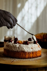 mano de hombre con cuchara terminando de preparar pastel dulce casero, azúcar en polvo espolvoreado con cerezas