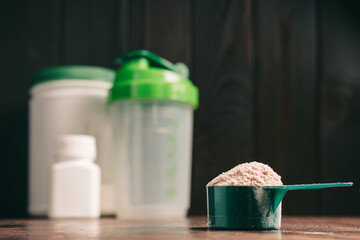 Chocolate whey protein powder in measuring spoon, shaker, plastic bottle on dark background. healthy eating, bodybuilding food supplements