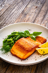 Seared salmon steak with green bean and lemons on wooden table
