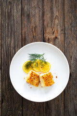 Seared cod loin and sliced lemon on wooden table
