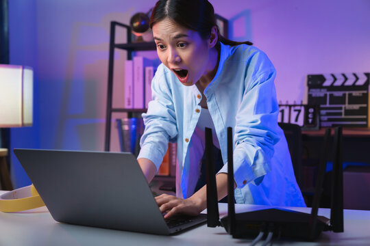 Young Asian woman open mouth with emotional excited and shocked amazed and looking at the laptop on the table in modern home office at night.