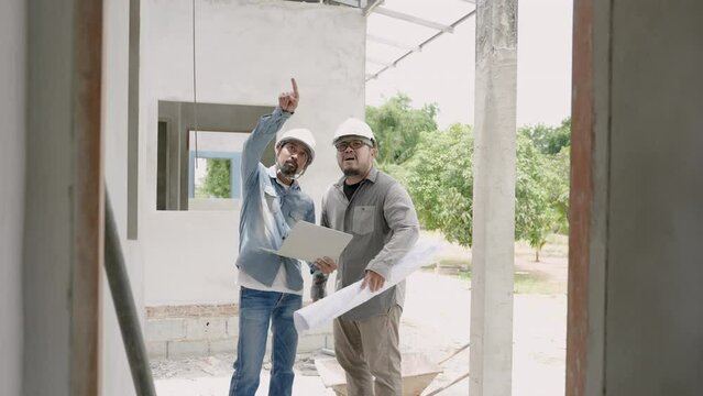 Indian engineer wearing a helmet Standing and inspecting house plans with the foreman. Follow plan in the blueprint. Let workers rush to build houses Requesting cooperation from people of multiracial