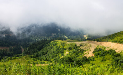 Fototapeta premium A beautiful dramatic landscape - green hillsides and mountains among white clouds and a space to copy on a summer day in Krasnaya Polyana in Russia