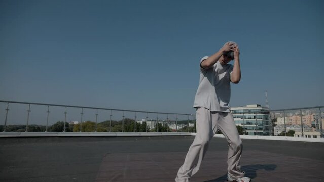 The guy coolly dances breakdance on the roof of the house. A man dances an energetic athletic dance.