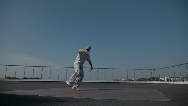 The guy coolly dances breakdance on the roof of the house. A man dances an energetic athletic dance.