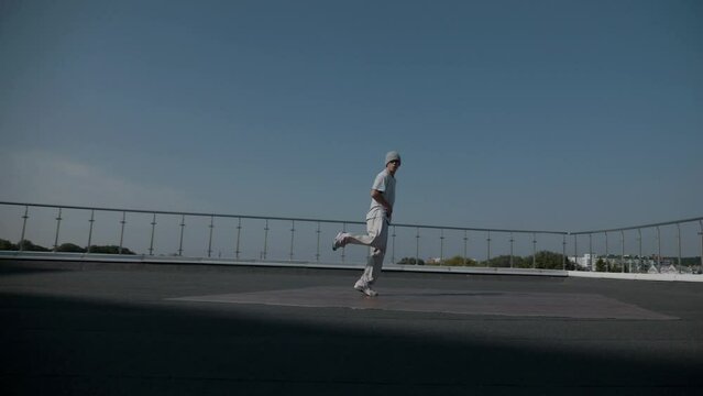 The guy coolly dances breakdance on the roof of the house. A man dances an energetic athletic dance.