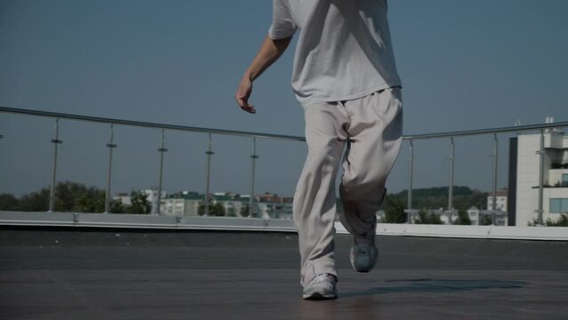 The guy coolly dances breakdance on the roof of the house. A man dances an energetic athletic dance.