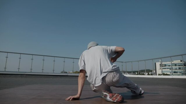 The guy coolly dances breakdance on the roof of the house. A man dances an energetic athletic dance.	

