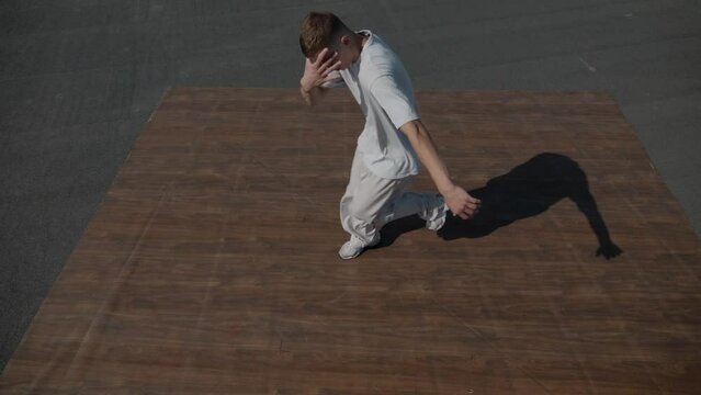The guy coolly dances breakdance on the roof of the house. A man dances an energetic athletic dance.	
