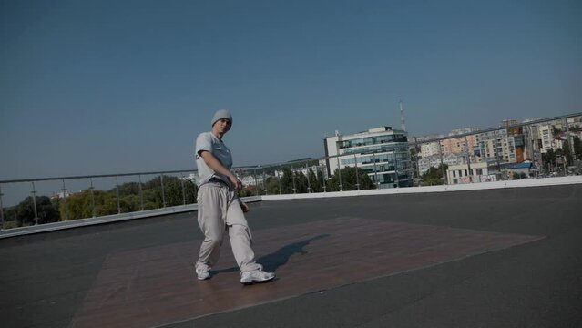 The guy coolly dances breakdance on the roof of the house. A man dances an energetic athletic dance.	
